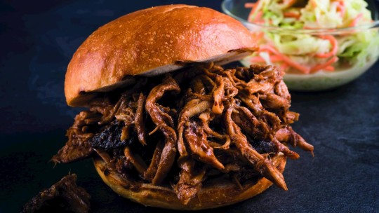 Nahaufnahme eines Pulled-Pork-Sandwichs mit zerrissenem Schweinefleisch und Barbecuesauce, serviert mit Krautsalat