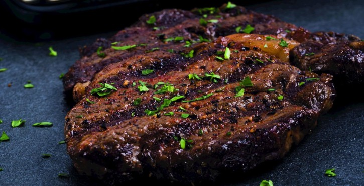 Um close-up de bifes grelhados decorados com ervas frescas picadas em uma superfície escura.