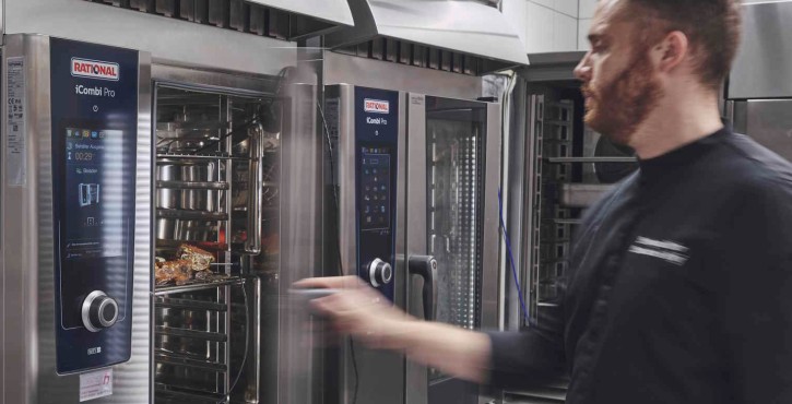 A chef in a black uniform operates an iCombi Pro oven in a kitchen, loading trays while checking the display.